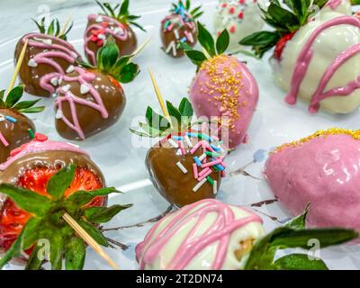 Erdbeeren in Schokolade. Süßes Dessert, appetitliche Beeren in Schokolade mit Streuseln. Mehrfarbige Beeren mit verschiedenen Dekor, selbst machen Stockfoto