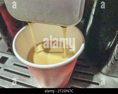 Rote Pappkaffeetasse, in die morgens köstlicher, heißer amerikanischer Kaffee aus der Kaffeemaschine im Büro gegossen wird. Stockfoto