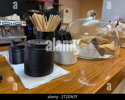 Einweg-Sticks aus Naturholz zum Mischen von Zucker in Tee oder Kaffee, Zuckerschale, Thermodeckel aus Kunststoff für Tassen und Kuchen an der Bar in einem kleinen Café. Stockfoto