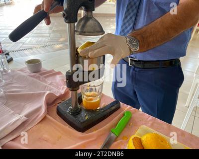 Bei der Herstellung von frisch gepresstem gelben Orangensaft drückt ein Mann in einem Hotel in einer warmen östlichen tropischen Kuh mit seinen Händen Saft in ein Glas Stockfoto