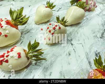 Erdbeeren in Schokolade auf Marmorhintergrund. Süßes Dessert, köstliche Beeren in Milchschokolade mit Zuckerstreuseln in Form von ihm Stockfoto