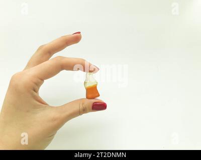 Marmelade-Bonbons. Ein Mädchen mit einer roten Maniküre hält Süßigkeiten in Form einer Flasche mit Limonade. Süße Zuckerbonbons in Form einer Cola-Flasche. Stockfoto