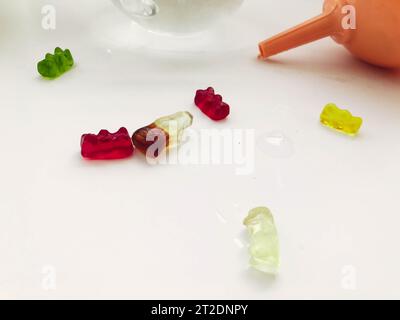 Gummiartige, gelatineartige Bären liegen auf einem feuchten, weißen, matten Hintergrund. Süße Süßigkeiten sind neben der Gießkanne. Köstliches kalorienreiches Dessert. Zuckerstreuung Stockfoto