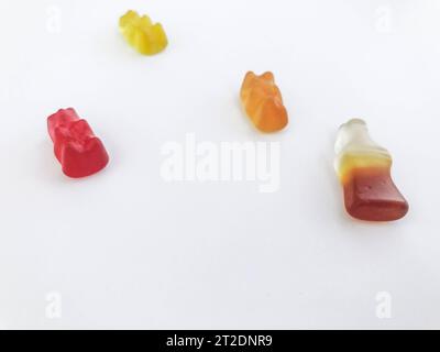 Gummibären auf weißem mattem Hintergrund. Rot, gelb und orange liegen auf dem Tisch. Daneben Marmelade in Form einer Flasche Limonade. swe Stockfoto