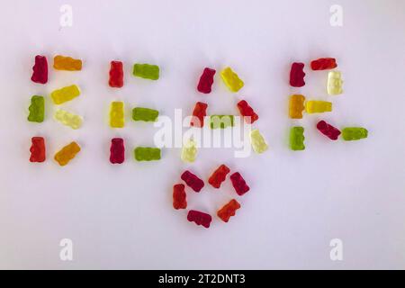 Wort aus Gummibären. Wortbär aus mehrfarbigen gelatineartigen Süßigkeiten. Neben herzförmigen Süßigkeiten. Appetitliche, kreative Schriftzüge. Ein essbares W Stockfoto