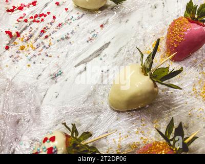 Erdbeeren in Schokolade auf Marmorhintergrund. Süßes Dessert, appetitliche Beeren in milchiger weißer Schokolade. Beeren in der Werkstatt, auf Zahn aufgereiht Stockfoto