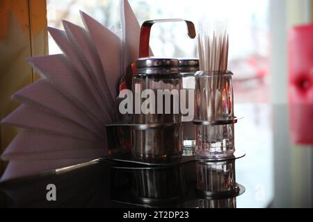 Glas Pfeffer- und Salzstreuer, Zahnstocher und Servietten auf dem Tisch im Café vor dem Fenster abends. Stockfoto