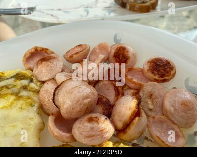 Herzhaftes, köstliches kalorienreiches Frühstück mit Bratwürsten, Würstchen in Scheiben auf einem Teller mit Eiern und Omelett. Stockfoto
