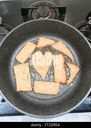 Roggenbrot wird in einer Pfanne in Öl, Croutons, Suhariki in Form von Herz gebraten. Stockfoto