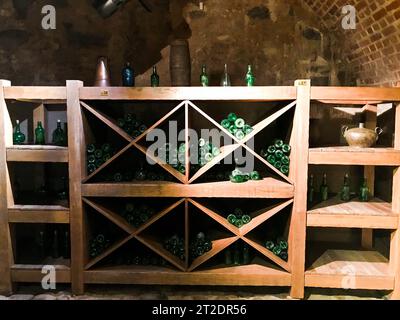 Alte grüne leere Wein- und Bierglasflaschen in einem Weinschrank mit Regalen in einem alten mittelalterlichen gemauerten Steinkeller. Stockfoto