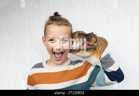 Das Kind spielt mit dem farbenfrohen Tyronosaurus-Dinosaurierkopf, der dem Jungen lustig ins Ohr beißt Stockfoto