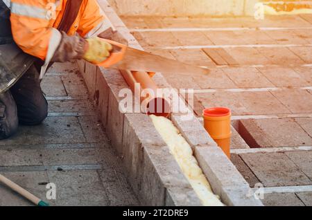 Bauherr schneidet Kunststoffrohre mit Handsäge während der Konstruktion des internen und externen Abflusssystems des neuen Hauses Stockfoto