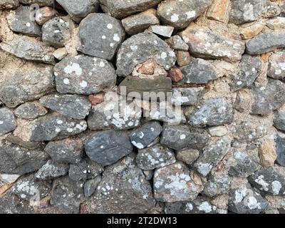 Hintergrund, Textur, Steinwand aus runden Steinen Kopfsteinpflaster natürliche Oberfläche natürlich scharf konvex Rohsteinpflaster mit Rissen. Stockfoto
