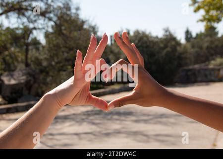 Hände verschiedener Ethnien, afrikanisch und europäisch, bilden mit ihren Fingern ein Herz. Vorstellung von Liebe, Freundschaft, Gleichheit Stockfoto