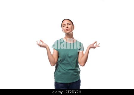 Die 30-jährige schlanke europäische Brünette mit einem Pferdeschwanz-Haar in einem grünen T-Shirt meditiert Stockfoto