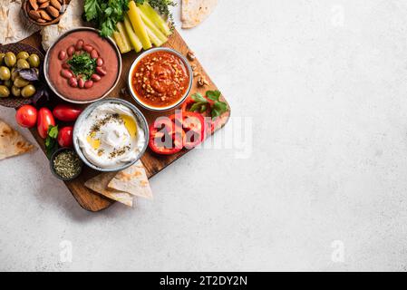 Arabische Mezze-Platte - foul, Labneh-Joghurt, Muhammara-Dip mit Pitabrot, Oliven und Gemüse auf weißem Hintergrund, Draufsicht, Kopierraum. Mittlere eas Stockfoto