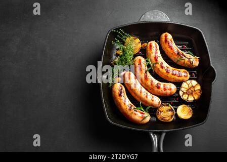 Gegrillte Würstchen mit Knoblauch und Kräutern auf gusseiserner Grillpfanne auf schwarzem Hintergrund, Kopierraum. Geröstete hausgemachte deutsche Würstchen. Stockfoto