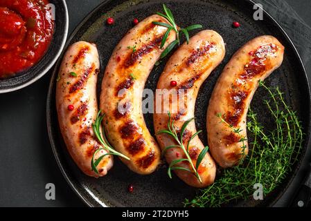 Gegrillte Würstchen mit Gewürzen und Kräutern auf schwarzem Hintergrund aus nächster Nähe. Gebratene hausgemachte Würstchen auf Teller. Stockfoto