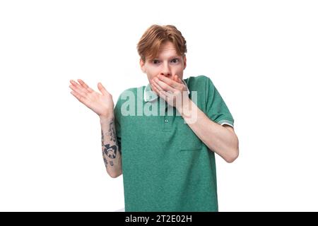 Junger überraschter Ingwermann mit einem Tattoo auf dem Arm, gekleidet in einem grünen Kurzarm-T-Shirt, ist schockiert Stockfoto