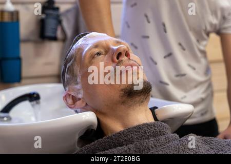 Ein Mann wäscht sich die Haare, während er einen Friseur besucht. Ein Friseur wäscht die Haare eines Kunden vor einem Haarschnitt in einem Schönheitssalon. Männerfrisur im Friseur Stockfoto