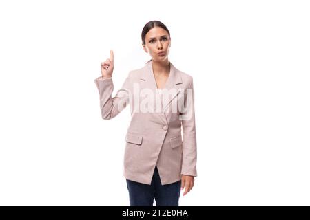 Eine angenehme junge Frau mit schwarzen Haaren in einer Jacke steht nachdenklich auf einem weißen Hintergrund mit Kopierraum Stockfoto