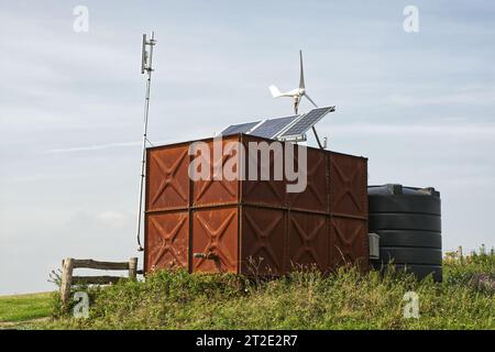 Photovoltaik-Solarpaneele und Windgenerator an Wassertanks in ländlicher Umgebung. England. Stockfoto