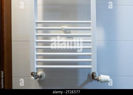 Weißer elektrischer Handtuchtrockner für das Badezimmer, an einer Wand mit Fliesen montiert Stockfoto