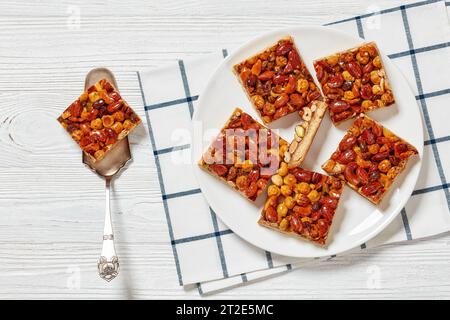 Hausgemachte Toffee gemischte Nüsse Shortbread Bars auf weißem Teller auf weißem Holztisch mit Kuchenschaufel, horizontaler Blick von oben, flacher Lagenplatz, freier Platz Stockfoto