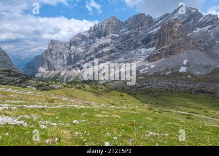 Imposante Bergkette mit einsamem Kalkstein butte in der grünen Graswiese darunter. Wunderschöne Gipfel der Dolomiten im Frühsommer Stockfoto