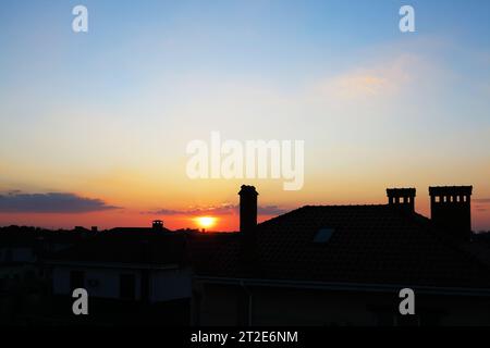 Sonnenuntergangshimmel über Odessa, Stadtlandschaft. Dunkle, klare Silhouetten von Häuserdächern mit Schornsteinen und Rohren im Sonnenschein. Stockfoto