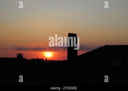 Sonnenuntergangshimmel über Odessa, Stadtlandschaft. Dunkle, klare Silhouetten von Häuserdächern mit Schornsteinen und Rohren im Sonnenschein. Stockfoto