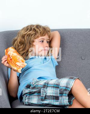 Ein Kind beißt eine große Scheibe frisch zubereiteter Pizza ab. Kleiner Junge, der Pizza isst. Der süße kleine Junge isst Pizzen. Teenager, der Pizza hält. Kind köstlich Stockfoto