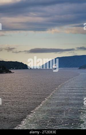 Blick vom Achterdeck der Fähre über den Oslofjord mit Kreuzfahrtschiff, Bergen und Wäldern in Norwegen. Wake Water Trail of Waves. Urlaubsreisekonzept Stockfoto