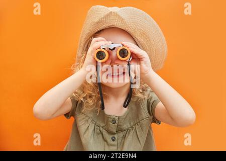 Das Mädchen schaut durch ein Fernglas auf orangefarbenem Hintergrund. Reise ins Ausland in freie Freizeit Erholung Get Away Flug Reise Konzept Stockfoto