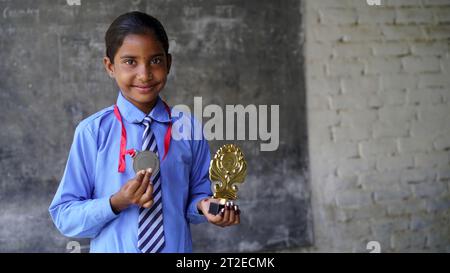 Porträt eines glücklichen Schulmädchens in Schuluniform, das die Siegtrophäe in der Hand feiert. Bildungskonzept. Skill india. Kinderträume Stockfoto