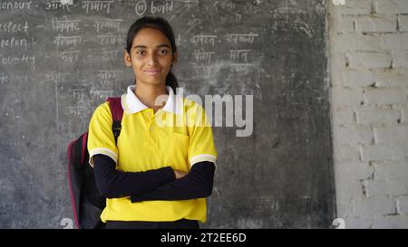 Lächelndes indisches Schulmädchen mit Rucksack und Blick in die Kamera. Fröhliches Mädchen in Schuluniform mit einem großen Lächeln. Grund- und Grundschule Stockfoto