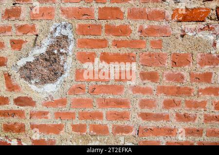 Die Textur des alten antiken mittelalterlichen antiken Steins, der hart abblättert, zerrissene Ziegelwand aus rechteckigen roten Tonziegeln und großen Steinen, Kopfsteinpflaster. T Stockfoto