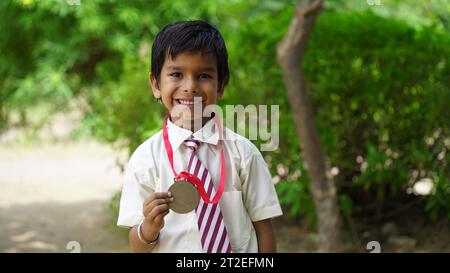 Porträt eines glücklichen Schuljungen in Schuluniform, der die Siegtrophäe in der Hand feiert. Bildungskonzept. Skill india. Kinderträume Stockfoto