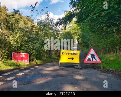 Schilder weisen darauf hin, dass eine Landstraße gesperrt ist und dass eine Umleitung erfolgt. Aufgenommen in Derbyshire, Großbritannien im Spätsommer. Stockfoto