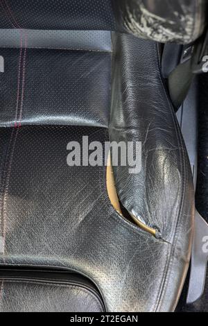 Gerissener und gerissener Autositz aus Naturleder. Beschädigtes Leder, freiliegender Schaum. Nahaufnahme, keine Leute Stockfoto