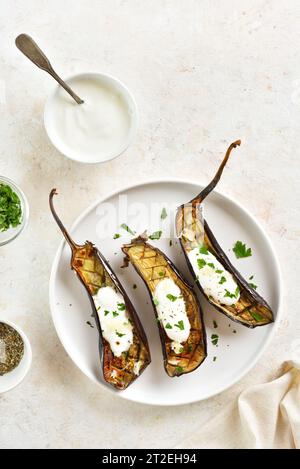 Im Ofen geröstete Aubergine mit Knoblauch-Joghurt-Dressing auf Teller über hellem Steinhintergrund. Draufsicht, flach Stockfoto