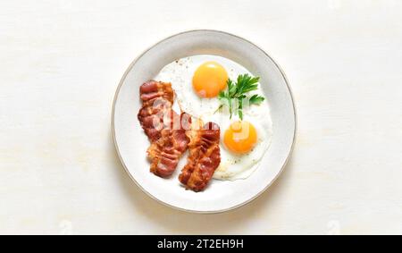Spiegeleier mit Speck auf Teller über hellem Steinhintergrund mit freiem Platz. Draufsicht, flach Stockfoto