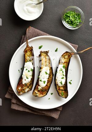 Gebackene Aubergine mit Knoblauch-Joghurt-Dressing auf Teller auf dunklem Hintergrund. Draufsicht, flach Stockfoto