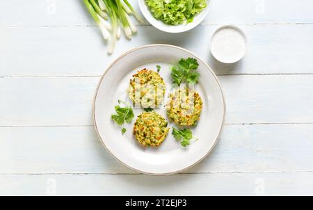 Vegetarische Gemüsezucchini-Pfannkuchen mit grüner Zwiebel auf Teller mit Soße über hellem Holzhintergrund. Draufsicht, flach Stockfoto