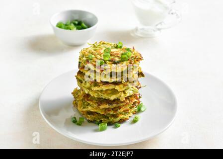 Stapel Zucchini-Krapfen. Vegetarische Gemüsezucchini-Pfannkuchen auf Teller über hellem Hintergrund. Stockfoto