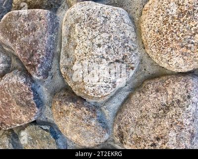 Textur aus natürlichem, geschnitztem massivem, rauem, scharfem, mineralgrauem braunem Stein mit Kopfsteinpflaster an den Felswänden. Steinhintergrund Stockfoto