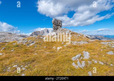 Großer freistehender Kalkstein auf einem kleinen Hügel, der von braunem Gras bedeckt ist, vor blauem Himmel mit Wolken Stockfoto