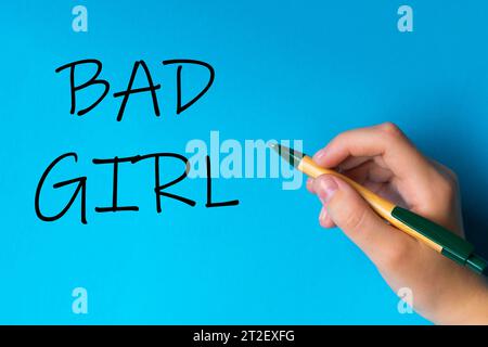 Kinder Hand mit Stift schreiben auf blauweißem Hintergrund. Schreibhand. Worte Bad Girl Stockfoto