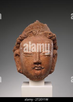Kopf eines Bodhisattva China (Xinjiang Autonomous Region) 6.–7. Jahrhundert die feine Modellierung von Haar und Gesicht vermittelt einen Eindruck von der raffinierten skulpturalen Produktion in Rawak. Frühe Fotografien zeigen, dass dieser Bodhisattva ursprünglich einen aufwendigen Topknoten hatte, der auf die Figur des zukünftigen Buddha Maitreya hindeutet. Dieser Bodhisattva hatte auch Blumen in seinen Haaren, Ohrringe und einen aufwendigen Halo, der mit mehreren Buddha-Bildern verziert war (ähnlich 30.32.33 und 30.32.44). Die Verwendung von ungebranntem rotem Ton ist ein technisches Merkmal, das mit spätafghanischen buddhistischen Bildern geteilt wird. Stockfoto