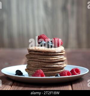 Ein Stapel Pfannkuchen mit frischen Himbeeren und Blaubeeren auf einem hellen Teller auf einem hölzernen Hintergrund Stockfoto